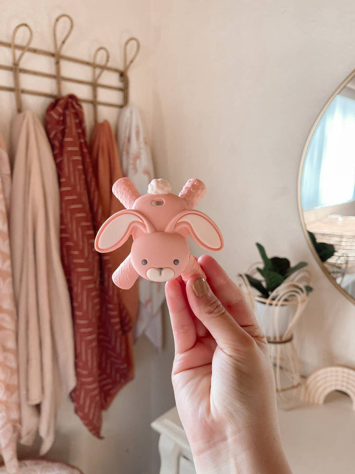 Hand holds pink Itzy Ritzy bunny teether, designed for baby molars, sustainably made for teething relief and eco-conscious comfort.